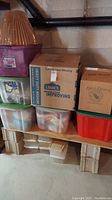 Overview of stacked storage boxes and totes containing holiday and home decor items including lamp shade and basket