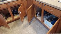 Kitchen corner cabinets with doors open showing multiple pots, pans, and bakeware items stored inside.