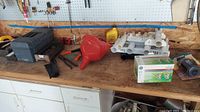 Workbench surface showing multiple tools including metal rod holders, red plastic funnel, boxed hardware, and other tools scattered on wooden surface.