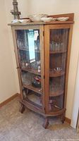 Full view of vintage wood framed glass door curio cabinet with curved glass front, wooden shelves inside, and carved wooden legs.