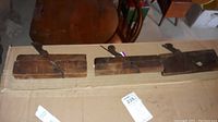 Three vintage wooden hand planers displayed on a cardboard surface, showing their worn wooden bodies and metal blades angled for concave shaping.
