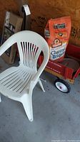 White plastic lawn chair in front of a red Radio Flyer wagon with a bag of charcoal briquettes behind.