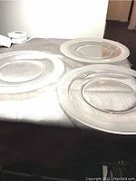 Top-down image of three textured glass dinner plates laid out on a beige surface, showing their translucent and textured rims and smooth centers.