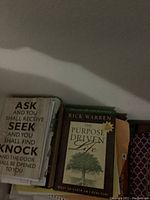 Books stacked including 'Ask and You Shall Receive' and 'The Purpose Driven Life' by Rick Warren visible on top.