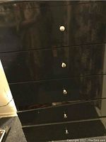 Front view showing chest drawers with metal knobs and glossy black finish.