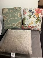 Three decorative pillows arranged together showing their colors and patterns: floral, beige textured, and blue-beige abstract pattern.