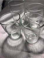 Photo showing 4 clear glass drinking glasses of different sizes arranged on a light-colored fabric surface.