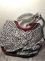 Front view of white and black leopard print large purse with red trim and large flower decoration on the front.