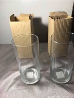 Two new clear cylindrical glass vases in front of their open cardboard boxes.