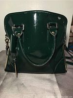 Front view of green shiny patent leather purse showing handles and slight surface wear.