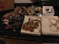 Photo showing a variety of gold-tone jewelry including bracelets and necklaces, plus two jewelry boxes containing a large amber stone set necklace and bracelet, and a delicate gold-tone bead set bracelet and necklace.