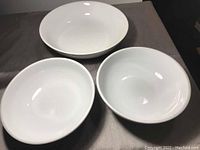 Three white ceramic bowls arranged on a gray surface showing top view; one larger and two smaller bowls