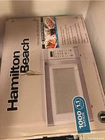 Box of Hamilton Beach microwave oven showing brand name, product image, and power specs at 1000 watts and 10 power levels