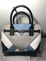 Front view of large structured Nine West purse with multicolored geometric panel design including light blue, gray faux crocodile texture, white and black sections, featuring black handles and silver clasp.