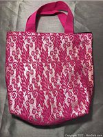 Front view of pink tote bag showing intricate lace floral pattern over light base fabric and dual pink fabric handles.