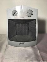 Front view of gray Aries portable electric space heater showing control knobs, mesh front heating grill, and branding.