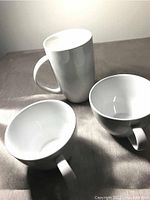 Top view of two white teacups and one tall white coffee mug showing interior and handles.