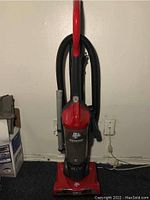 Front view of the red and black Dirt Devil Pro Express vacuum cleaner showing bagless canister and hose attachment, standing upright.