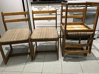 Three Mid-Century Modern teak chairs, two upright and one stacked, showing the overall style and condition including upholstery fabric.