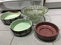 Four serving trays displayed on floor; two pottery with pale green and brown stripe, one brown pottery bowl, one green glass pedestal bowl.