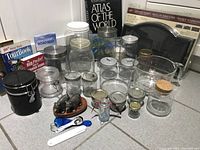 Photo showing glass jars of various sizes, ceramic fish salt and pepper shakers, black jar with latch lid, and measuring spoons, with travel books and maps in background.