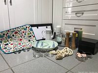 Photo showing the entire lot of kitchen items on floor including the tray, glasses, plates, grinders, jars, rope, and small containers.
