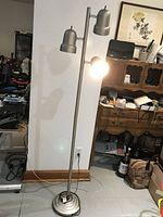 Full view of the chrome floor lamp standing upright with three lights, one turned on.