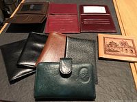 Photo showing 7 wallets and ID holders arranged on a wooden table, various colors including black, brown, maroon, green, and tan, showcasing the front and interior sides.