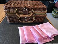 Closed picnic basket with four folded pink gingham napkins in front