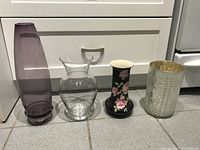 Four vases side by side showing different styles and colors: purple tinted, clear glass, black floral painted, textured clear with gold interior.