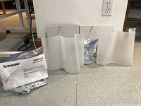 Two thick, frosted white glass wall mount shades with wavy design on floor with mounting plates and plastic bags of hardware.