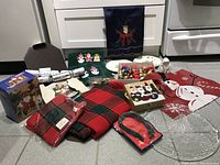 Photo of overall Christmas holiday linens and decor items on the floor, including tablecloth, napkins, towels, ornaments, and festive packaging.