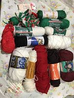 Overview photo showing multiple yarn skeins in red, white, green, black, and burgundy shades laid out on floral fabric background.