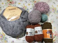 Overview of eight skeins of yarn varying in color, brand, and fiber content on floral background