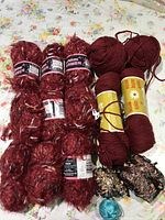 Full view of red yarn skeins including six textured skeins and two solid red skeins along with two multi-colored skeins and one teal skein.