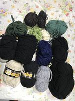 Overview of yarn skeins in various colors including black, green, cream, gray, and blue on floral background.