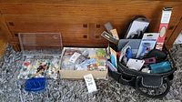 Overview of several plastic containers and boxes filled with assorted buttons and craft tools on a carpeted floor.
