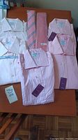 Overview of multiple new pink tone dress shirts and ties including folded shirts and two ties placed on table.