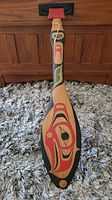 Full view of the front of the wooden paddle showing carved and painted Haida eagle design in red, black and green colors.
