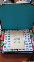 Open carrying case showing neatly arranged Mah Jong tiles, scoring sticks, dice, and booklet inside.