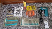 Full view of cordless drill, drill bits in plastic cases, wire wheel brushes and manual arranged on carpet