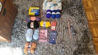 Full lot overview showing mini sewing machine, yarn skeins in multiple colors, knitting needles and accessories laid out on carpet