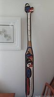 Full front view of entire carved and painted paddle hanging on wall