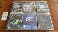Seven PS3 game cases on wood surface showing Grand Theft Auto and racing titles.