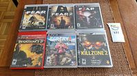 Six PS3 games displayed on a wooden table, showing cover art for FEAR, FEAR 2, FEAR 3, Resistance 2, Far Cry 4 Limited Edition, and Killzone 2.