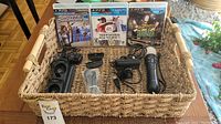 Photo showing 3 PS3 game cases and assorted PS3 controller accessories including chargers and cables placed in a woven basket