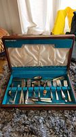 Full view of silver plated utensils in vintage wooden box with blue felt lining and satin lid.