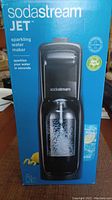 Front view of the boxed SodaStream JET sparkling water maker showing the machine and the carbonating bottle.