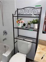 Metal over the toilet shelf installed above toilet with faux plants on shelves.