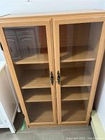 Front view of a wooden cabinet with two glass paneled doors and three shelves inside.
